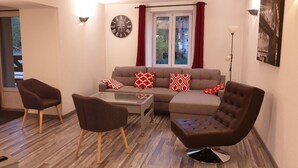 A living room with a sofa, two armchairs, a coffee table, a TV, and a clock on the wall. - Gîte de la Verdurette: Tranquil Stay in the Countryside (Pettonville)