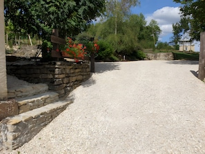 Un sendero de grava, muro de piedra, cruz de madera y flores rojas.
