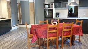 A modern kitchen with a dining table set for six, a coffee machine, and a microwave. - Gîte de la Verdurette: Tranquil Stay in the Countryside (Pettonville)