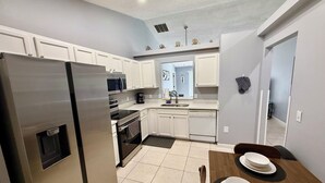 Une cuisine moderne avec des meubles blancs, des appareils en acier inoxydable et un coin repas comprenant une table et des chaises en bois.