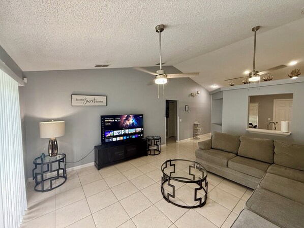 A living room with a TV, ceiling fans, a sofa, and a lamp. - Grand Superior Pines 3BR Pool Home near Disney (Four Corners)