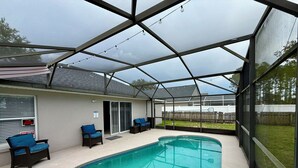 Une piscine extérieure couverte, dotée d’un patio, de chaises et offrant une vue sur le jardin arrière.