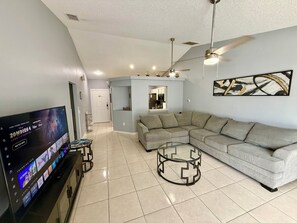 A living room with a sectional sofa, a glass coffee table, a flat-screen TV, and a ceiling fan. - Grand Superior Pines 3BR Pool Home near Disney (Four Corners)