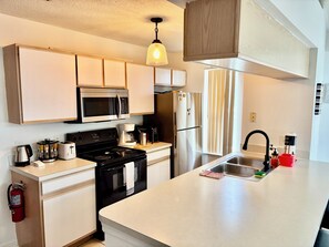 A modern kitchen with a stove, microwave, refrigerator, and a large island with a sink. - Grand Family Superior 3BR Condo near Disney (Four Corners)