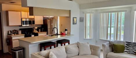 A modern kitchen with a central island, a dining area with a sofa, and a ceiling fan.