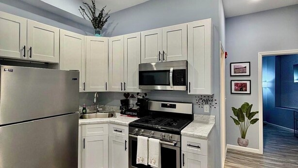 A modern kitchen with white cabinets, stainless steel appliances, and a coffee-themed floor mat.