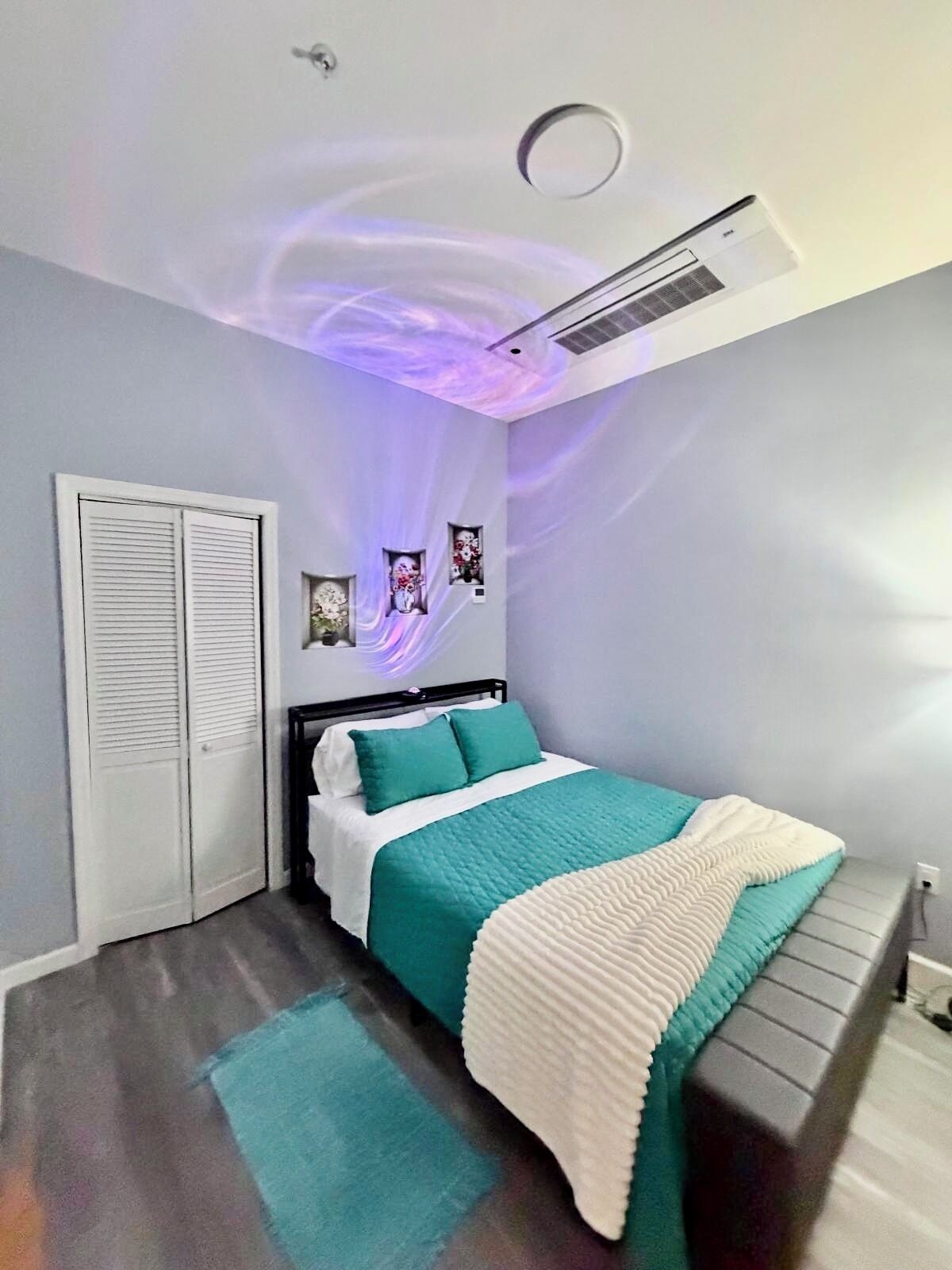 Ein Schlafzimmer mit Bett, Deckenventilator, Klimaanlage, Kleiderschrank und einem kleinen Fenster.