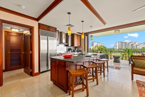 A modern kitchen with a large island, wooden cabinets, and a view of a balcony with outdoor furniture. - Hale Alani Resort-style Stay (Kapolei)