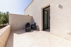 Un'area patio esterna con pavimento in pietra, due sedie in vimini e un tavolino.