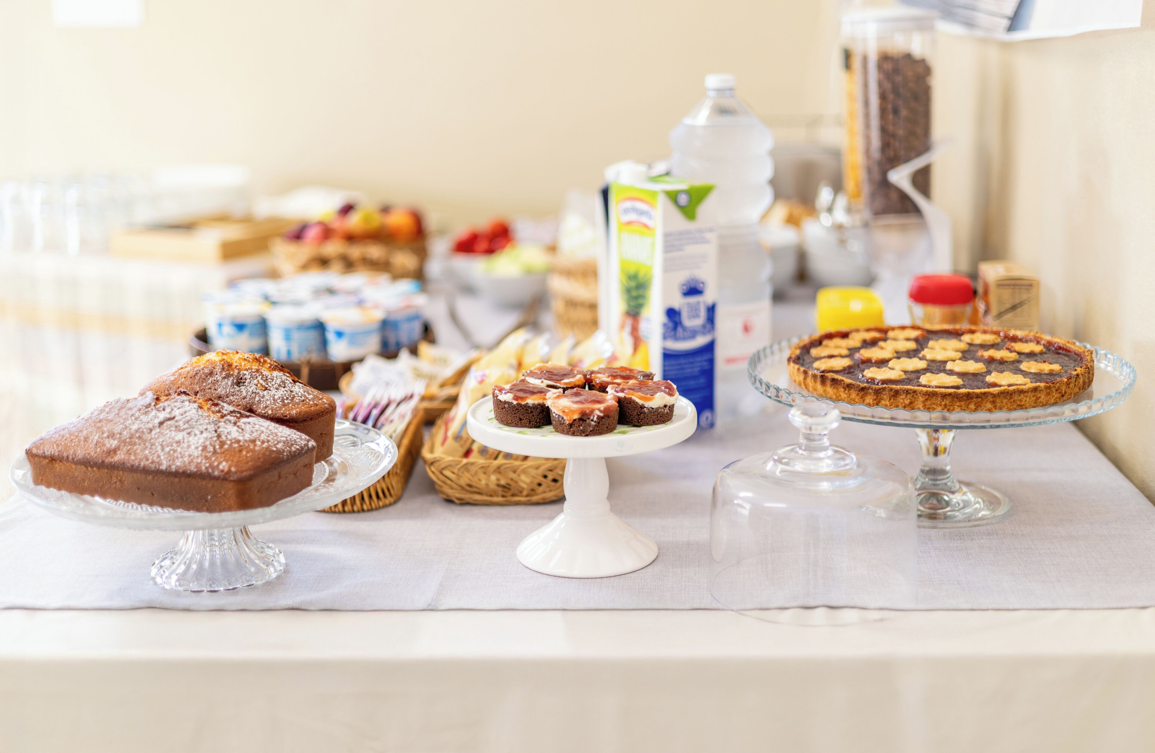 Una mesa con varios postres, incluyendo un pastel, un bizcocho y una tartaleta, sobre un mantel blanco.