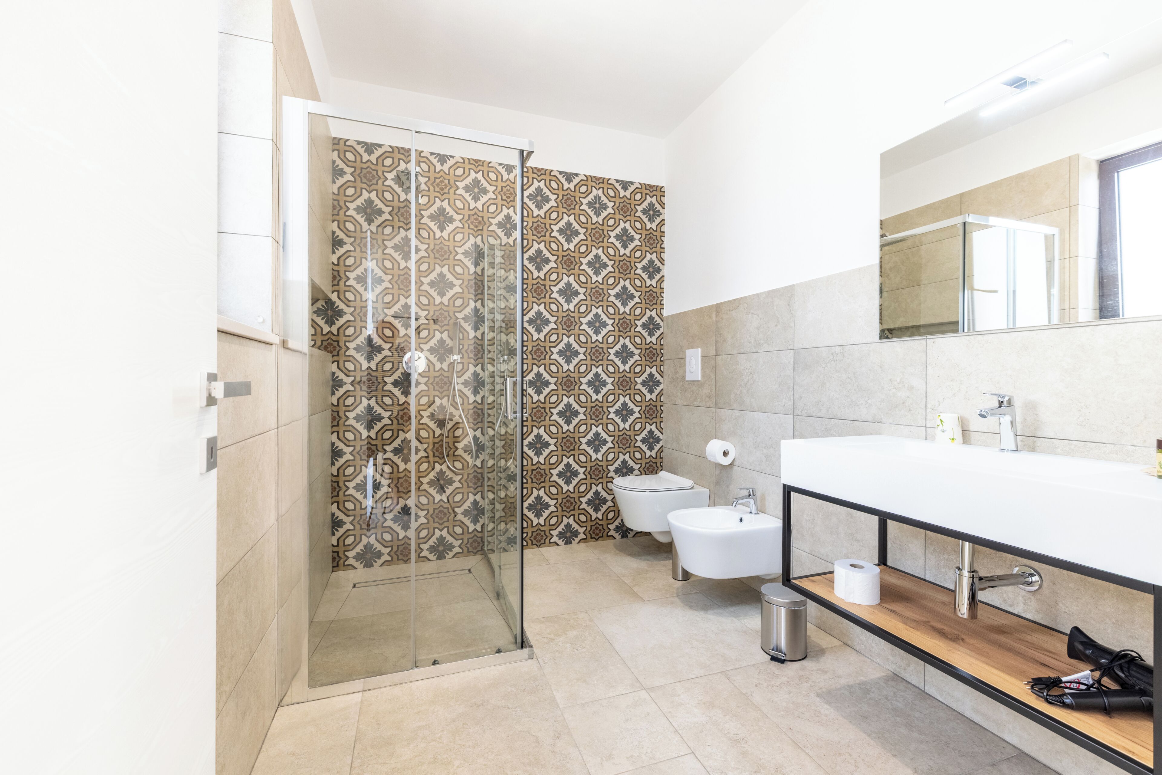 Ein modernes Badezimmer mit Duschkabine aus Glas, Toilette, Waschbecken mit Spiegel und Holzregal.