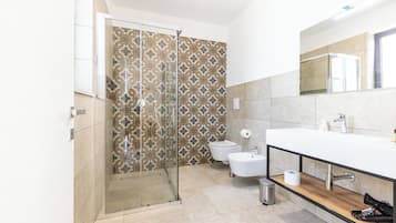 A modern bathroom with a glass shower enclosure, a toilet, a sink with a mirror, and a wooden shelf.