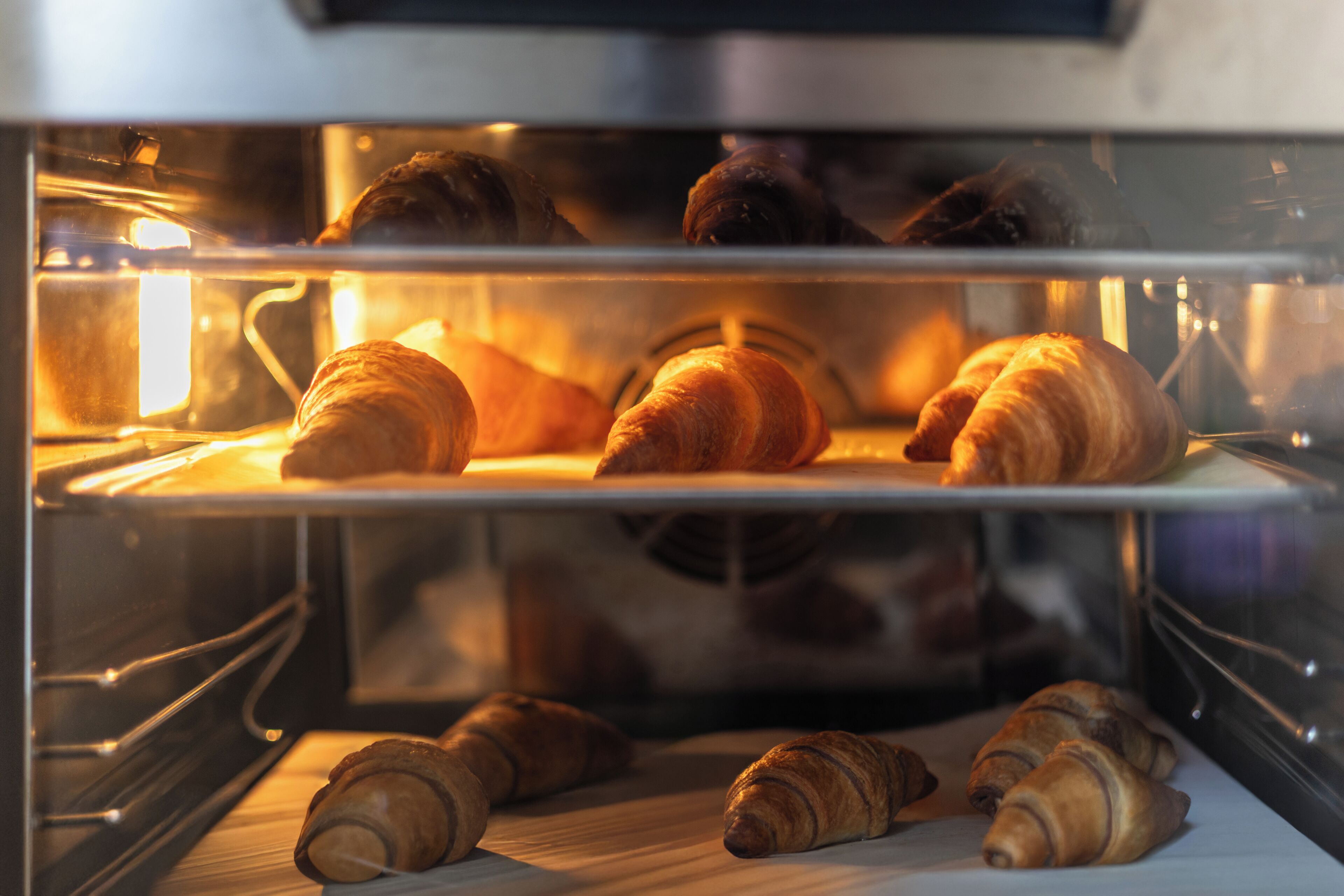 An oven with several croissants inside, indicating a bakery or kitchen setting.