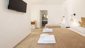 A hotel room with a flat-screen TV, a bed with a quilted cover, a bedside table with a lamp, and a bathroom visible through an open door. - Masseria Coccolo (Carovigno)