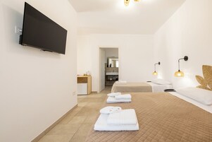 Una camera d'albergo con una TV a schermo piatto, un letto con copriletto trapuntato, un comodino con una lampada e un bagno visibile attraverso una porta aperta.