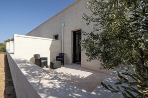 A modern building with a flat facade, a small outdoor seating area with two chairs and a table, and a large olive tree in the foreground. - Masseria Coccolo (Carovigno)