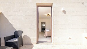 Una stanza con un letto, una sedia e un'apertura che conduce a un'altra stanza.
