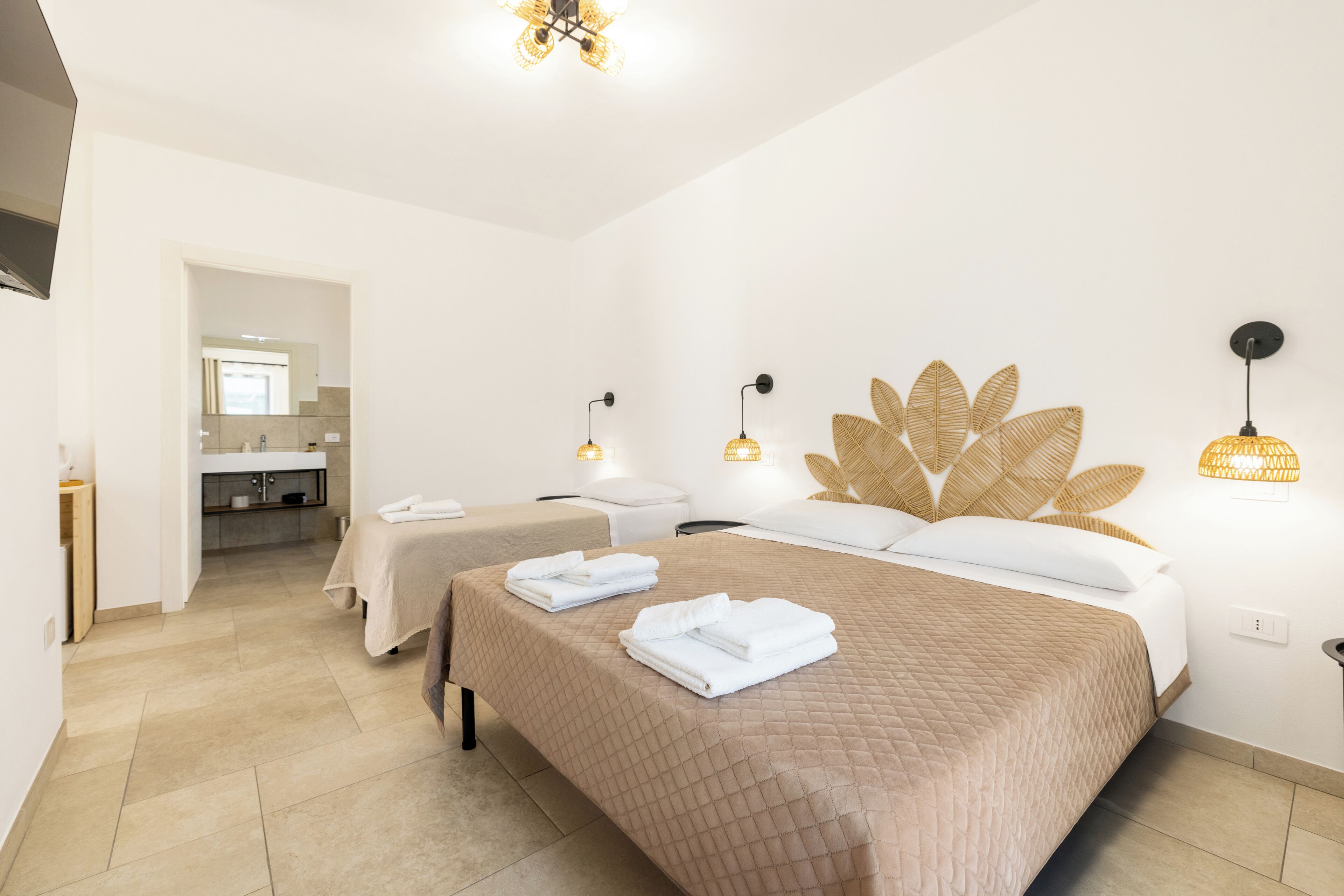 A hotel room with two beds, a bathroom, and a view of the hallway.