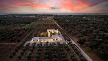 Vista aérea de una propiedad con un edificio central rodeado de olivares, campos y una carretera.