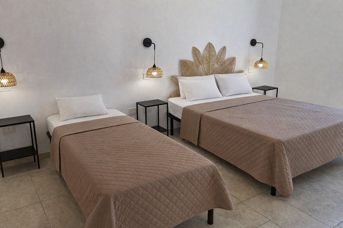 Deux lits simples avec des têtes de lit, des tables de chevet et des lampes fixées au mur.