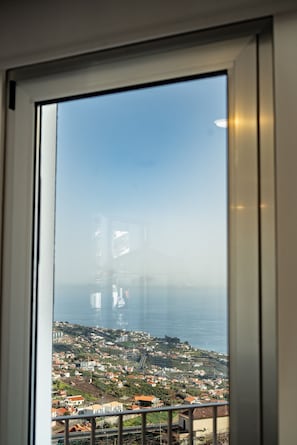 Vista a través de una ventana de un pueblo costero con edificios, un puente y el mar.