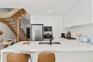 Eine moderne Küche mit weißen Schränken, einem Edelstahlkühlschrank, einem eingebauten Ofen und einem Gasherd.