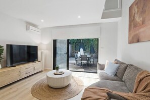 Ein modernes Wohnzimmer mit Flachbildfernseher, einer Couch, einem Couchtisch und einer Glasschiebetür, die auf eine Außenpatio führt.