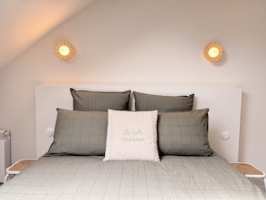 A bedroom with a bed, pillows, a bedside table, and a wall-mounted light fixture.