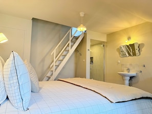 Une chambre à coucher avec un lit, un escalier, une salle de bain avec un lavabo et un miroir.