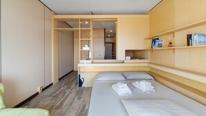 Ein modernes Hotelzimmer mit integriertem Kleiderschrank, einem Bett mit ordentlich gefalteten Handtüchern und einer kleinen Ablage mit Büchern.