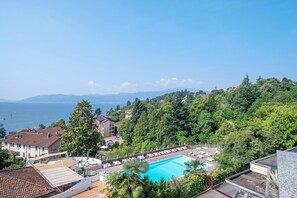 A pool area with lounge chairs, a view of the sea, and buildings surrounded by trees. - Apartment 'Bellavista Apartment' - Appartamento La Selva Vista Lago Ghiffa (Susello)