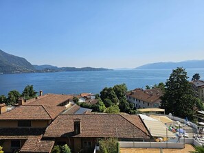 A coastal town with terracotta-roofed buildings, a marina with boats, and a clear view of the sea and distant mountains.