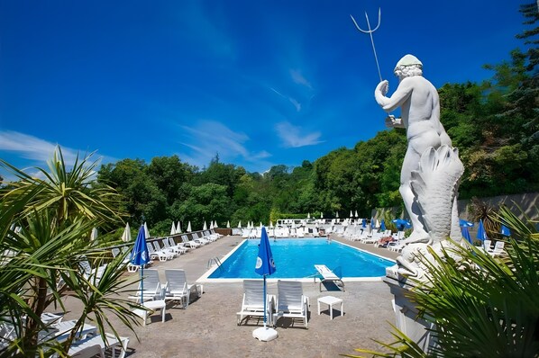 Ein Poolbereich mit Liegestühlen und Sonnenschirmen, umgeben von Pflanzen und einer Statue.
