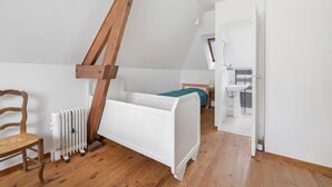 A bedroom with a sloped ceiling, a wooden chair, a white bed, a radiator, and a bathroom with a sink and mirror. - Gîte Chez Madeleine: Private Terrace, Garden, and Wi-Fi in Coutances (Coutances)