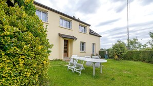 A two-story house with a garden, a white table and chairs, and a door. - Gîte Chez Madeleine: Private Terrace, Garden, and Wi-Fi in Coutances (Coutances)