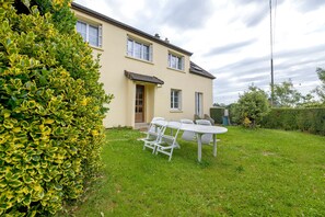 A two-story house with a garden, a white table and chairs, and a door. - Gîte Chez Madeleine: Private Terrace, Garden, and Wi-Fi in Coutances (Coutances)