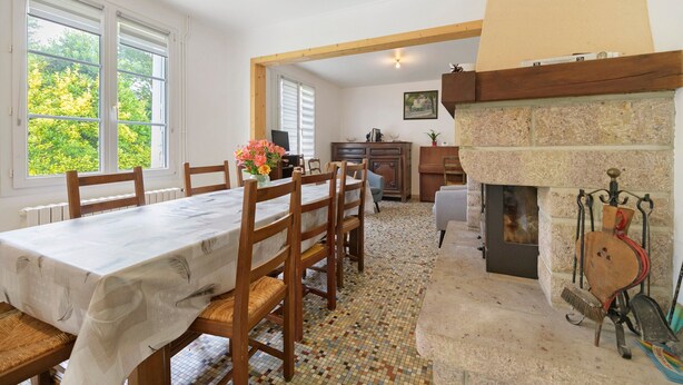 A dining area with a table set for six, a fireplace, and a view of trees through the windows. - Gîte Chez Madeleine: Private Terrace, Garden, and Wi-Fi in Coutances (Coutances)