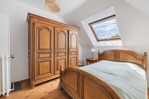 A bedroom with a wooden bed, a wardrobe, a small bedside table, a lamp, and a skylight. - Gîte Chez Madeleine: Private Terrace, Garden, and Wi-Fi in Coutances (Coutances)