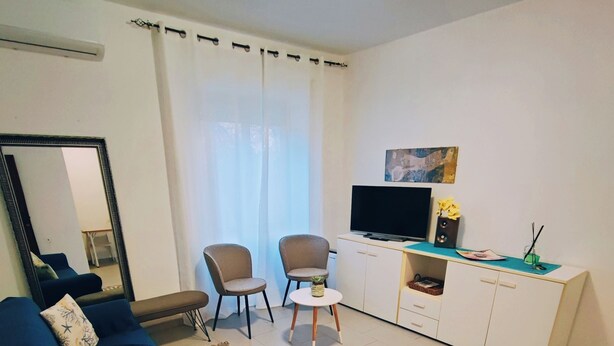 Ein Wohnzimmer mit einem blauen Sofa, zwei Sesseln, einem Couchtisch, einem Fernseher und einem weißen Schrank.