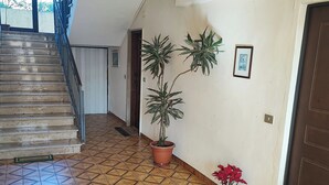 Ein Flur mit Treppe, gefliestem Boden, Topfpflanzen und einer Tür.