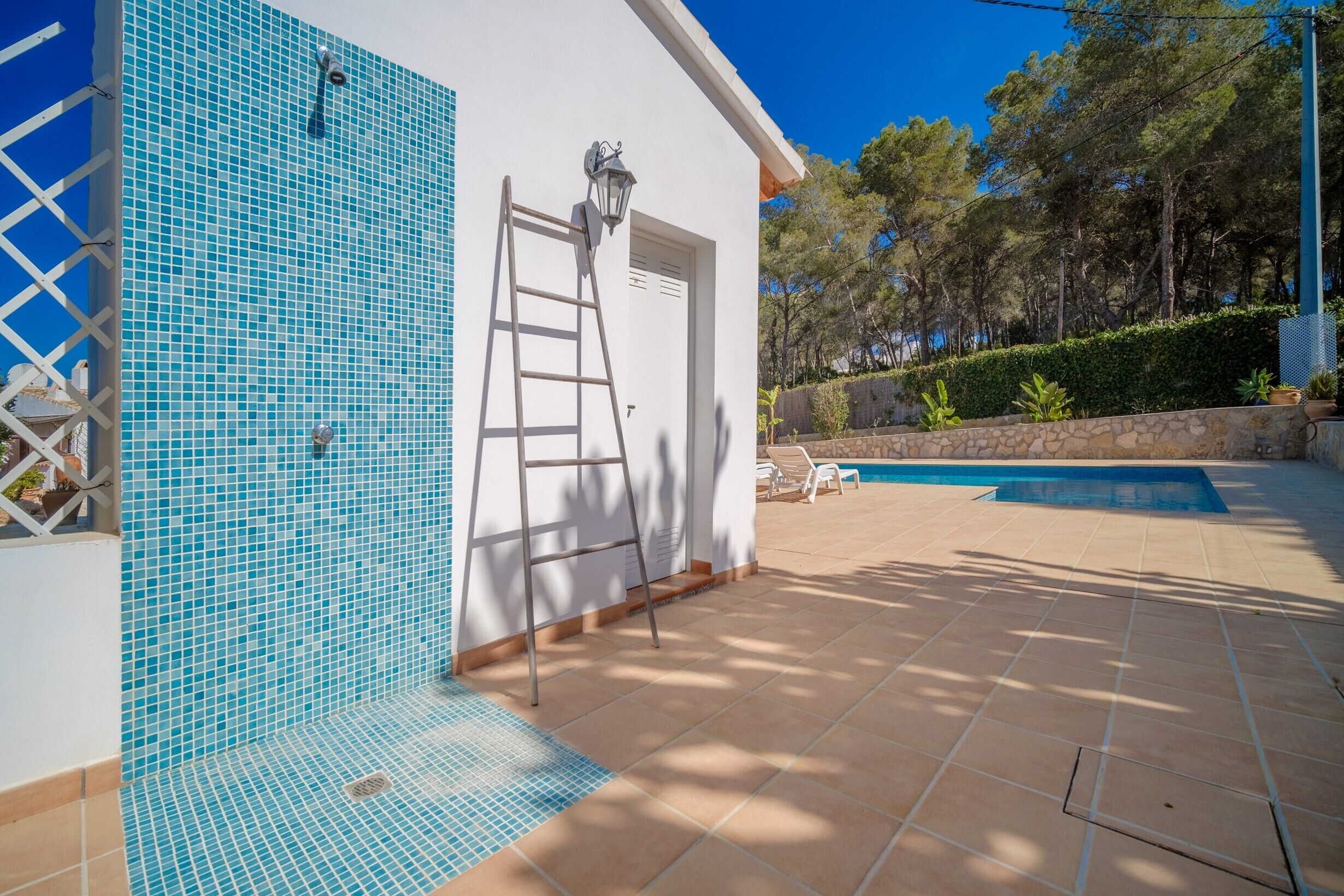 Zona de piscina con pared de azulejos, una escalera y una puerta.