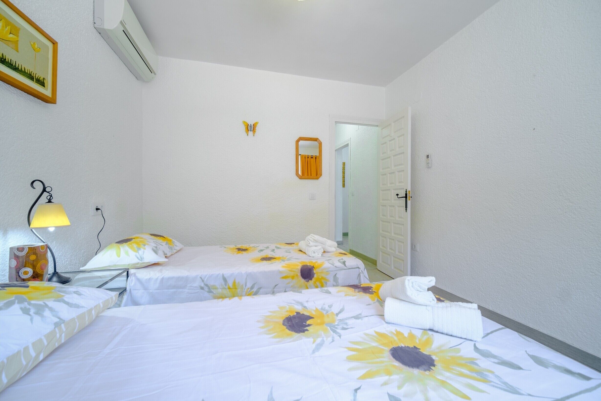 A hotel room with two beds, a lamp, a mirror, and a door.