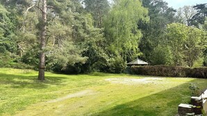Un’area verde con prato, un gazebo e fitti alberi, delimitata da un siepe.