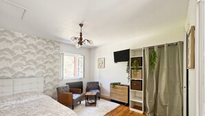 Una camera da letto con un letto, due poltrone, un tavolino, una televisione, un termosifone, una finestra e un armadio.
