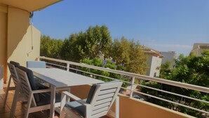 Un balcon avec une table et des chaises, une balustrade et une vue sur les arbres et les bâtiments.