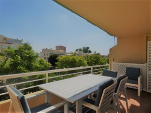 En balkon med et bord og stole, udsigt til bygninger og træer, og en væg med mønster.