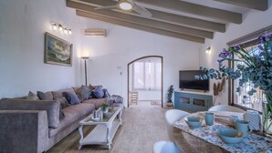 A living room with a sofa, coffee table, TV, and a dining area with chairs and a table. - Holiday Home 'Jávea - Just Steps from the Sea' with Private Terrace, Wi-Fi & AC (Jávea)