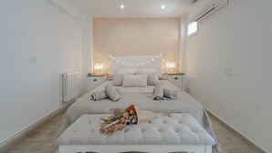 A bedroom with a large bed, bedside tables, a bench, and a wall-mounted air conditioner. - Holiday Home 'Jávea - Just Steps from the Sea' with Private Terrace, Wi-Fi & AC (Jávea)