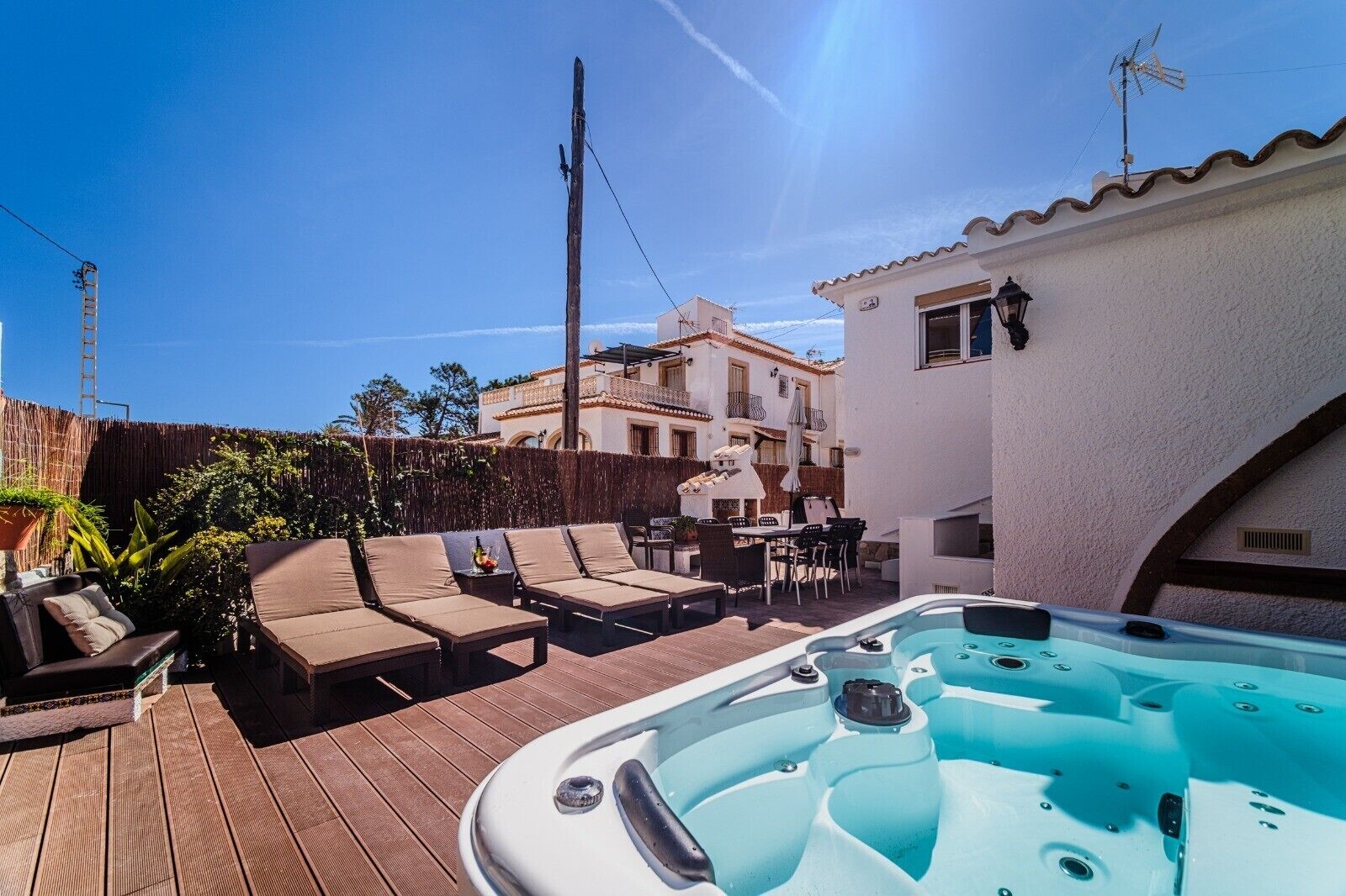 A wooden deck with lounge chairs, a hot tub, and a building with balconies.