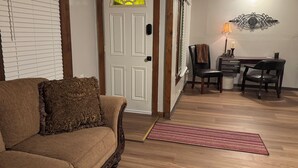 Una sala de estar con un sofá marrón, una puerta con ventana, un área de comedor con una mesa y sillas, y una alfombra roja en el suelo.